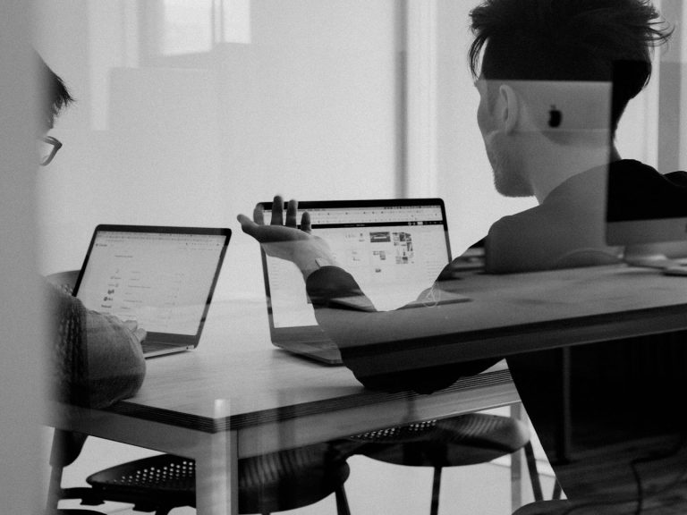 Two People Meeting Two people sitting at a table working on laptops, discussing ideas in a modern workspace.