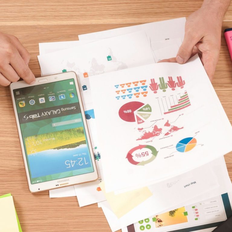 Printed Pages with Graphs - Marketing Development Hands holding a tablet and a printed report with colorful charts and graphs on a wooden table.